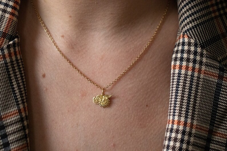 Op de afbeelding: Een gouden ketting met een klein hanger met een gestileerd zon- en wolkmotief.
