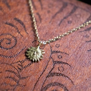 May include: A gold necklace with a sun pendant. The pendant features a detailed face with a textured surface.