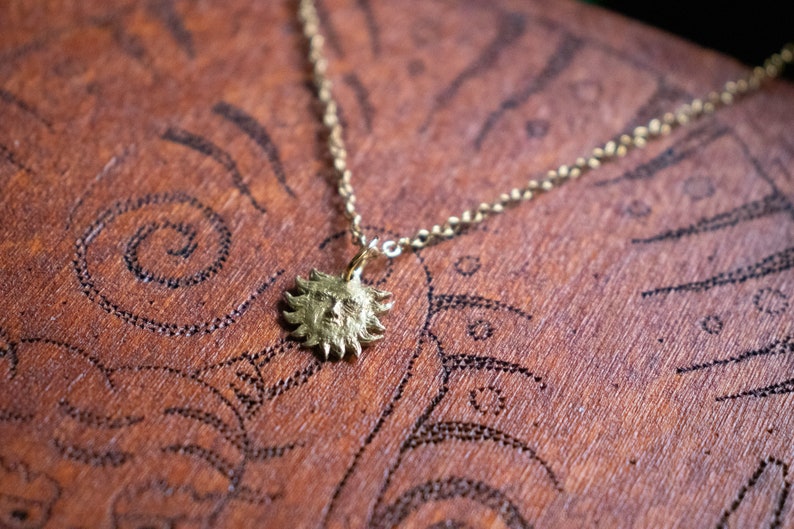 May include: A gold necklace with a sun pendant. The pendant features a detailed face with a textured surface.