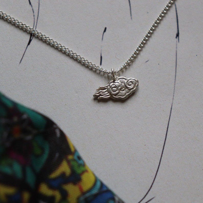 May include: A silver necklace with a cloud-shaped pendant. The cloud is detailed with swirling lines and has a delicate, whimsical design.