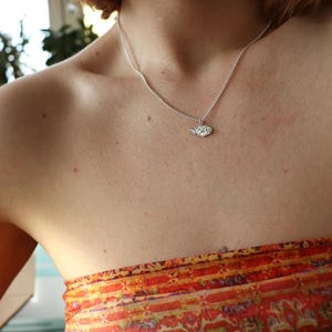 May include: A silver necklace with a small, detailed pendant. The pendant is shaped like a leaf and has a textured surface.