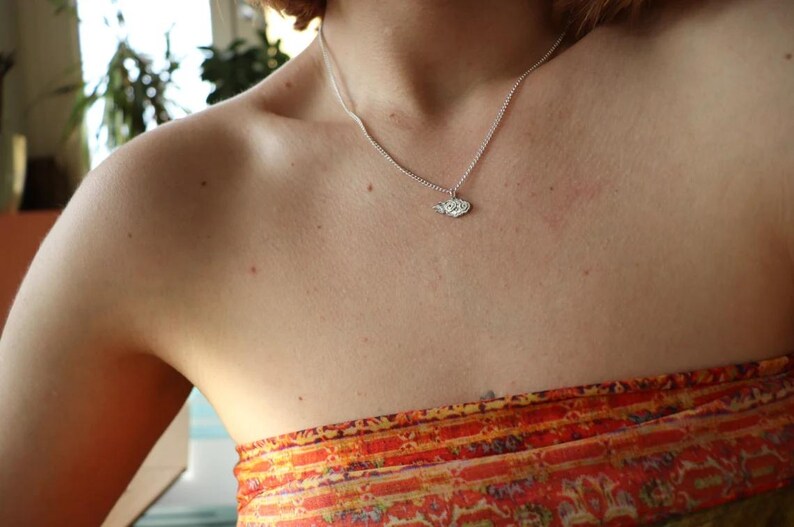 May include: A silver necklace with a small, detailed pendant. The pendant is shaped like a leaf and has a textured surface.
