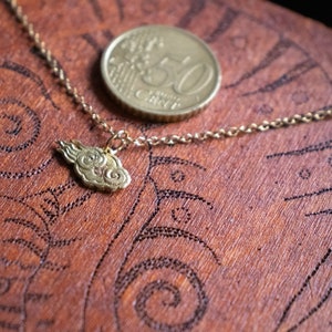 May include: A gold chain necklace with a cloud-shaped pendant. The necklace is lying on a wooden surface with a 50 cent coin.