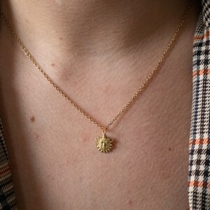 May include: A gold chain necklace with a small sun pendant. The pendant is detailed with a face and rays.