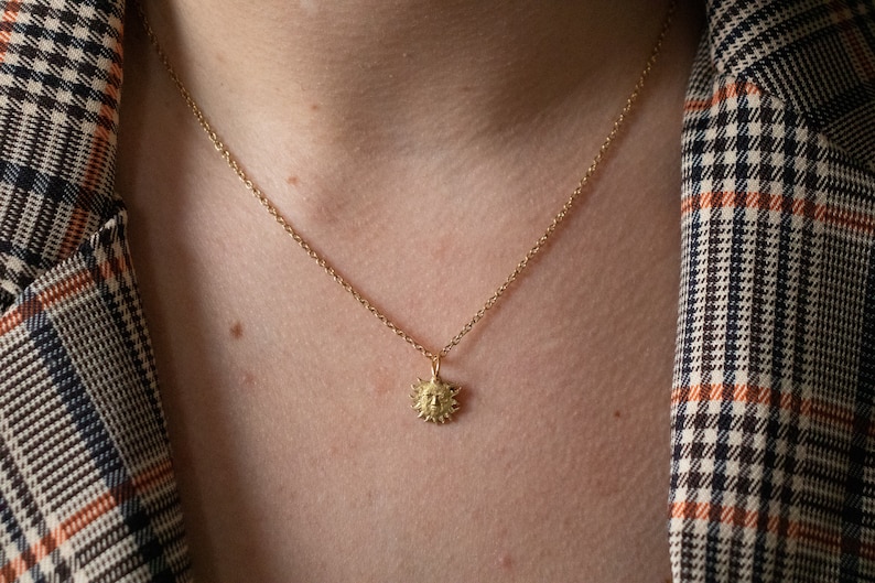 May include: A gold chain necklace with a small sun pendant. The pendant is detailed with a face and rays.