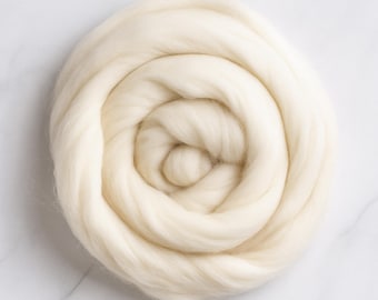 May include: A tightly coiled bundle of creamy white wool roving, ideal for fiber art projects. The soft, natural fibers are arranged in a spiral pattern, creating a visually appealing texture. The wool is a light, off-white color.