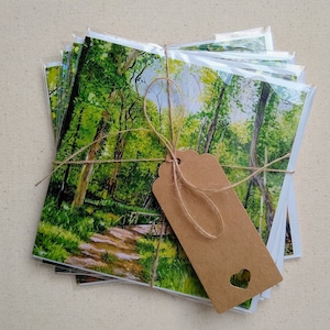 Könnte beinhalten: Ein Stapel leerer Grußkarten mit einem Aquarellbild eines Waldweges und einem braunen Papier-Geschenk-Etikett, das mit Schnur gebunden ist.