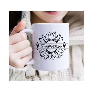 May include: White ceramic mug with a black and white sunflower design and the name "Stephanie" written in a script font inside the sunflower. The sunflower is surrounded by two black hearts.