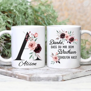 Könnte beinhalten: Zwei weiße Keramikbecher mit Blumendesigns. Ein Becher hat einen schwarzen Buchstaben A und den Namen Alison. Der andere Becher hat den Text "Danke, dass du mir beim Wachsen geholfen hast".