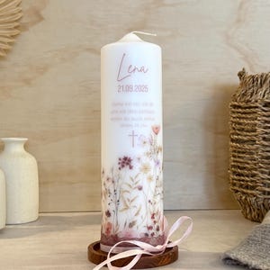 May include: A white cylindrical pillar candle featuring a floral print at the base, the name Lena, the date 21.09.2025, and the German text "Siehe ich bin mit dir und will dich beh&uuml;ten, wohin du auch ziehst. Moses 28,15a" with a cross symbol.