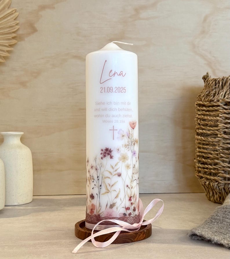 May include: A white cylindrical pillar candle featuring a floral print at the base, the name Lena, the date 21.09.2025, and the German text "Siehe ich bin mit dir und will dich beh&uuml;ten, wohin du auch ziehst. Moses 28,15a" with a cross symbol.