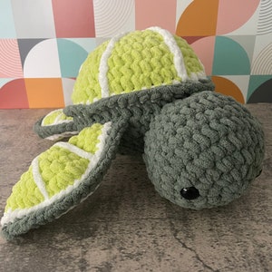 May include: A crocheted green and white turtle plush toy. The turtle has a green shell with white stripes and a green body with black eyes.