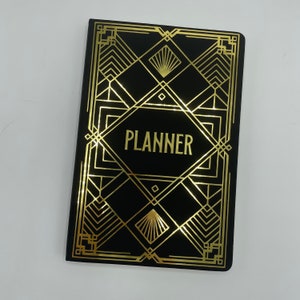 May include: Black planner with a gold art deco design and the word "PLANNER" in gold lettering.