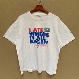 以下が含まれることがあります： 赤と青で「I ATE WHERE IT ALL BEGAN」の文字が入った白い斑点模様のTシャツ。シャツには、建物の小さな画像と「BIRTHPLACE OF KENTUCKY FRIED CHICKEN」の文字も表示されています。