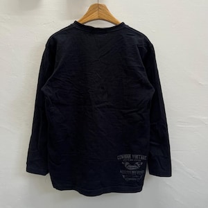 May include: Black long-sleeved top with a crew neck. The shirt has a faded graphic on the lower back that reads "GENUINE VINTAGE" and "CUSTOM MACHINES". The top is hanging on a wooden hanger.
