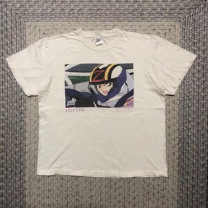 Peut inclure: T-shirt blanc avec un imprimé graphique d'un personnage de dessin animé portant un casque et conduisant une voiture de course. Le texte "BLEED KAGA" est imprimé sous l'image.