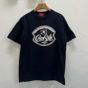 Puede incluir: Camiseta negra de cuello redondo con un gráfico blanco. El gráfico presenta las palabras "Cream Soda" en una fuente estilizada, con el texto "Too Fast To Live Too Young To Die" en la parte superior. Las palabras "Trade Mark 1967" están debajo.
