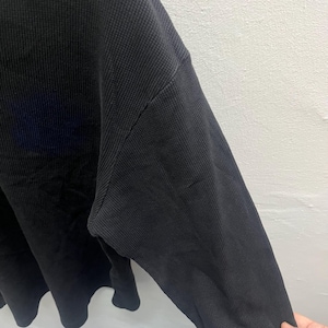 May include: A long-sleeved shirt made of a black waffle-knit fabric. The garment features a textured grid pattern throughout the material, a crew neckline, and a relaxed fit with dropped shoulder seams that extend down the arm to the sleeve.