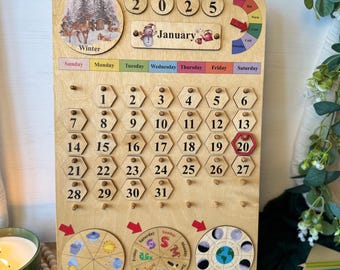 May include: Wooden perpetual calendar with a winter scene, the year 2025, and the month of January. Features numbered date tiles, weather, moon phase, and day of the week indicators. The calendar is made of light-colored wood.
