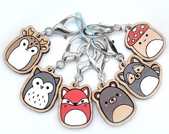 May include: A set of seven wooden keychains featuring various woodland animals and a mushroom. Each keychain has a silver metal clasp and a cute cartoon animal design. The animals include a deer, owl, fox, bear, and raccoon.