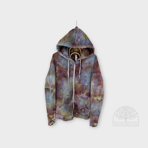 Pode incluir: Um moletom com capuz com zíper tie-dye em tons de azul, roxo e marrom pendurado em um cabide de madeira. O moletom com capuz tem um capuz com cordão, um zíper completo e dois bolsos frontais. O logotipo OAKSTREET DYE é visível no canto inferior direito.