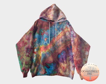Pode incluir: Uma jaqueta de moletom tie-dye em tons de vermelho, roxo, azul, verde e amarelo. A jaqueta tem um grande bolso na frente e um capuz com cordão. A jaqueta é feita pela Oak Street Dye e tem o texto "One of a Kind" e "Oak Street Dye" em uma etiqueta circular.