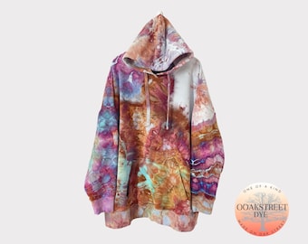 Pode incluir: Um moletom tie-dye em tons de laranja, rosa, azul e branco. O moletom tem um capuz grande e um bolso canguru. O moletom está pendurado em um cabide contra um fundo branco. O texto "OOAKSTREET DYE" é visível em uma etiqueta circular anexada ao moletom.