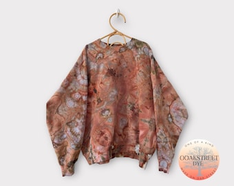 Pode incluir: Uma camisola cor de ferrugem com um padrão floral, tingida à mão com uma técnica de tie-dye. A camisola tem um decote redondo e mangas compridas. A etiqueta na camisola diz "OOAKSTREET DYE MADE ON OAK STREET ONE OF A KIND".
