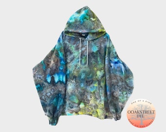 May include: A tie-dye hoodie in shades of blue, green, and brown with a large pocket on the front. The hoodie has a drawstring hood and is made by Oak Street Dye.