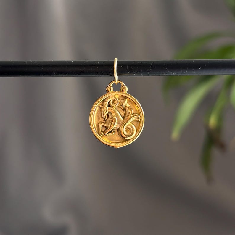 Może przedstawiać: Złoty wisiorek z symbolem zodiaku Koziorożca. Okrągły wisiorek ma szczeg&oacute;łowy relief z motywem kozła i gwiazdy. Wisiorek jest zawieszony na małej pętli, gotowy do dodania do naszyjnika lub bransoletki.
