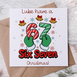 Könnte beinhalten: Weihnachtskarte mit dem Text "Luke have a Six Seven Christmas!". Die Zahlen 6 und 7 werden von grünen behandschuhten Händen gehalten. Die Karte hat Schneeflocken, Glocken und einen braunen Umschlag.