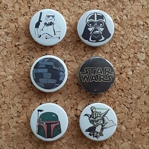 Puede incluir: Seis pines de botón con temática de Star Wars. Los pines muestran a Darth Vader, un Stormtrooper, la Estrella de la Muerte, las palabras "Star Wars", Yoda y Boba Fett.