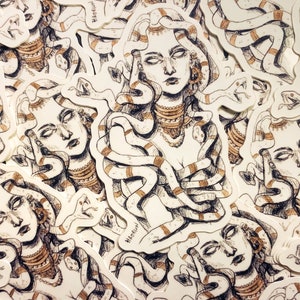 Op de afbeelding: Een verzameling Medusa-stickers. Elke sticker toont een gedetailleerde illustratie van Medusa met slangen als haar, versierd met sieraden. Het kunstwerk is in bruine en witte tinten, met een handgetekende esthetiek.