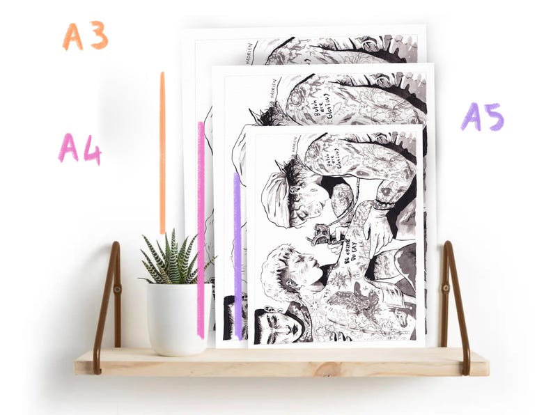May include: Three black and white illustrations of people with tattoos, printed on white paper and framed with white borders. The illustrations are displayed on a wooden shelf with a small potted plant.
