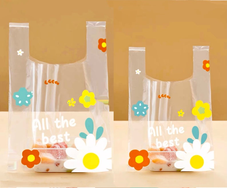 Puede incluir: Dos bolsas de pl&aacute;stico transparentes con asas, con un dise&ntilde;o floral colorido y el texto "All the best". Las bolsas est&aacute;n vac&iacute;as y listas para llenarse con regalos o golosinas.