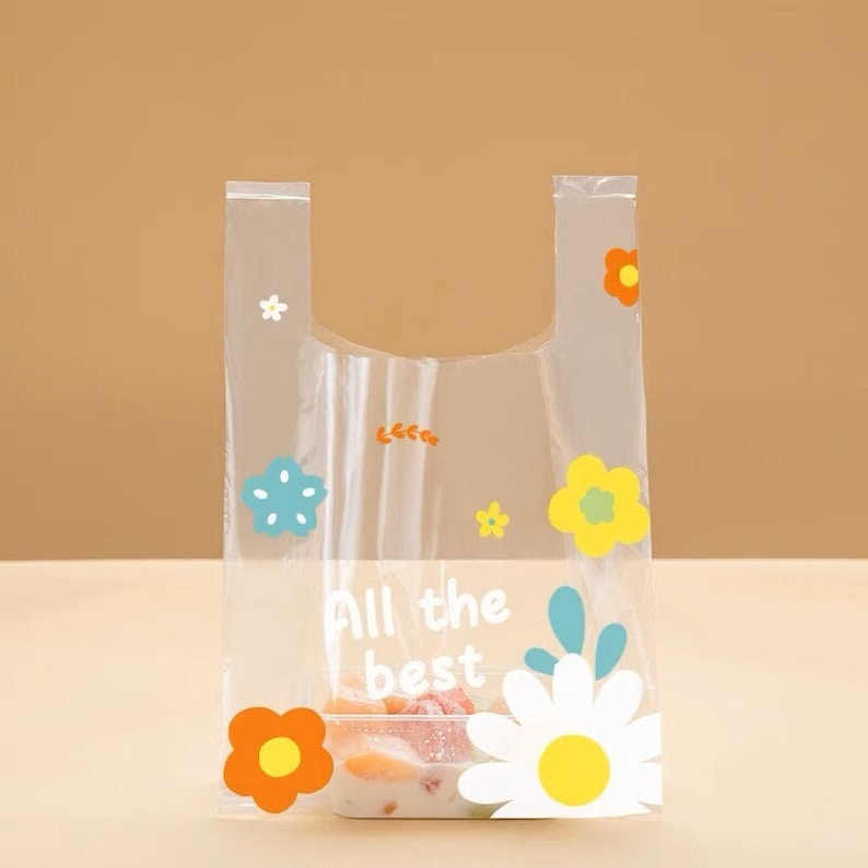 Puede incluir: Una bolsa de pl&aacute;stico transparente con un dise&ntilde;o floral y el texto "All the best". La bolsa est&aacute; llena de fruta y tiene un fondo blanco.