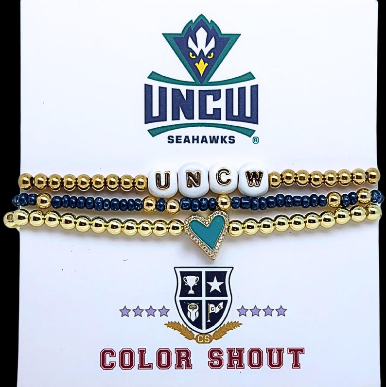 May include: Three beaded bracelets with gold and navy blue beads. One bracelet spells out "UNCW" with white letter beads. A teal heart charm is on one bracelet. The card reads "UNCW Seahawks" and "Color Shout".