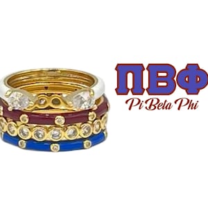 May include: Four gold rings with white, maroon, and blue enamel. The rings are set with small clear stones and are stacked on top of each other. The rings are labeled with the Greek letters "ΠΒΦ" and the words "Pi Beta Phi".