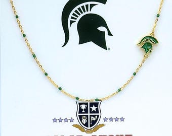 Könnte beinhalten: Eine goldfarbene Halskette mit grünen Akzenten und einem grünen Spartanerhelm-Anhänger. Die Halskette hat eine Reihe kleiner grüner Perlen und ein Schildemblem mit dem Text "COLOR SHOUT". Der Hintergrund zeigt ein großes Spartanerhelm-Logo.