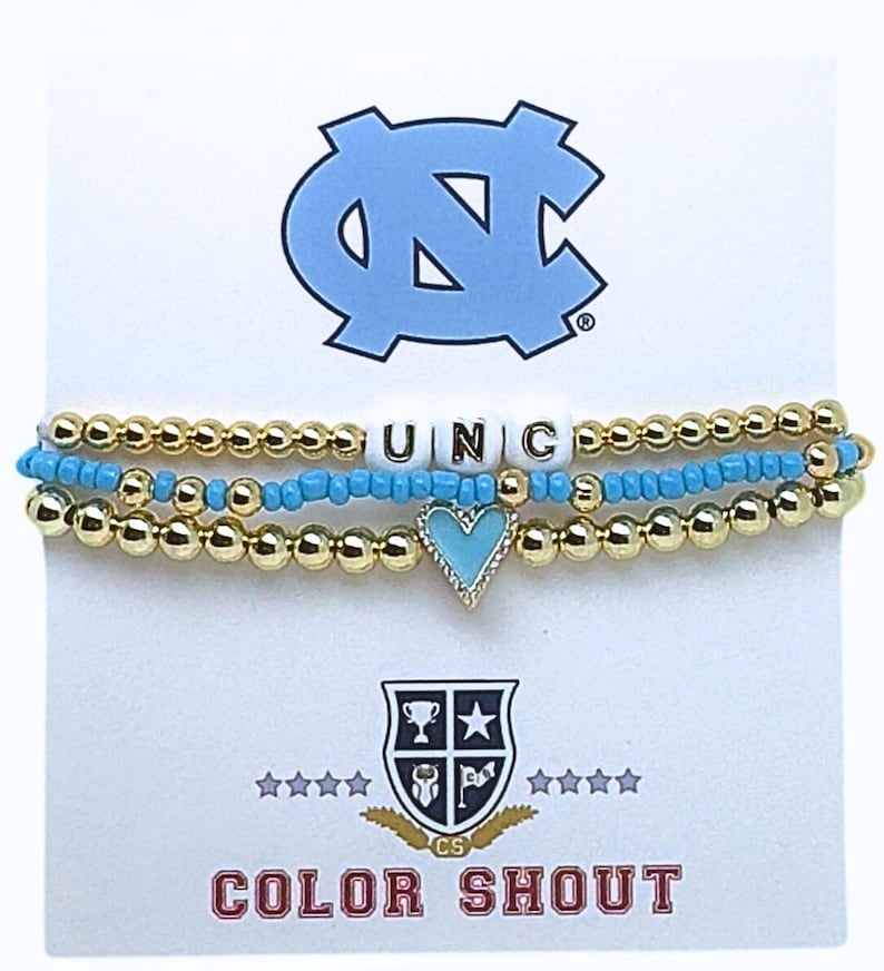 May include: Three beaded bracelets with gold and turquoise beads. One bracelet spells out "UNC" with white letter beads. A light blue heart charm is on one bracelet. The bracelets are displayed on a white card with a light blue logo and the text "COLOR SHOUT".