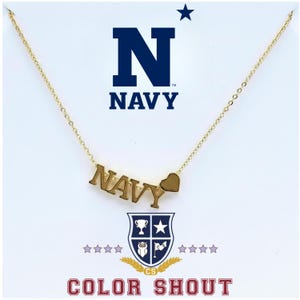 May include: A gold-toned necklace featuring a pendant that spells out the word NAVY in capital letters, accompanied by a small gold heart charm. The necklace is displayed against a white background with the text NAVY and COLOR SHOUT.