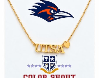 May include: A gold-toned necklace featuring the letters UTSA in a block font with a small heart charm attached to the right side. The necklace is displayed on a white card with a blue and orange bird logo, a shield emblem, and the text COLOR SHOUT.