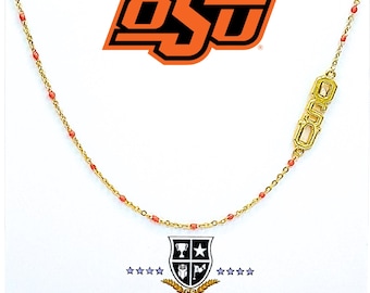 Könnte beinhalten: Goldkette mit kleinen roten Perlen und einem goldenen Anhänger mit den Buchstaben "OSU" in einer Schreibschrift. Die Kette liegt auf einem weißen Hintergrund mit einem Logo für "Color Shout" am unteren Rand.