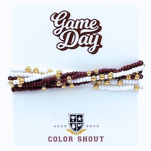 May include: Stackable beaded bracelets in white, maroon, and gold. The bracelets are displayed on a white card with the words "Game Day" in a script font. The card also features a logo and the words "COLOR SHOUT".