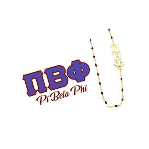 May include: A gold-colored necklace with the Greek letters ΠΒΦ, and small red beads. The necklace also features the text "Pi Beta Phi" in a blue and brown design. The jewelry is displayed on a white background.