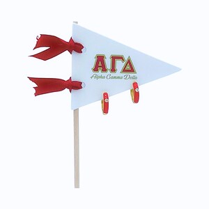 May include: Red and gold hoop earrings with a single clear stone on each earring. The earrings are displayed on a white pennant with the letters "AGA" and the words "Alpha Gamma Delta".