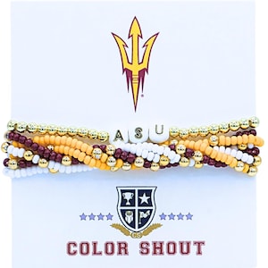 May include: A beaded bracelet with the letters "ASU" in white beads. The bracelet features gold, maroon, white, and yellow beads. The background includes a trident logo and the words "COLOR SHOUT".