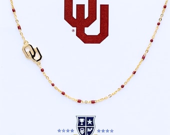 May include: A gold-toned chain necklace featuring small, evenly spaced dark red enamel beads and a gold-toned OU logo charm. The image includes a large red OU logo at the top and a shield-shaped logo with the text COLOR SHOUT at the bottom.