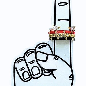 May include: A white foam finger with a black outline and the Texas Tech University logo. Several rings are displayed on the foam finger, including a ring with a clear stone and a red band, and a black band ring.