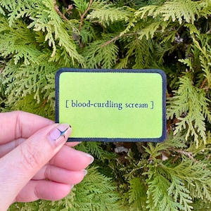 May include: A green and black embroidered patch with the text "[blood-curdling scream]" in black.